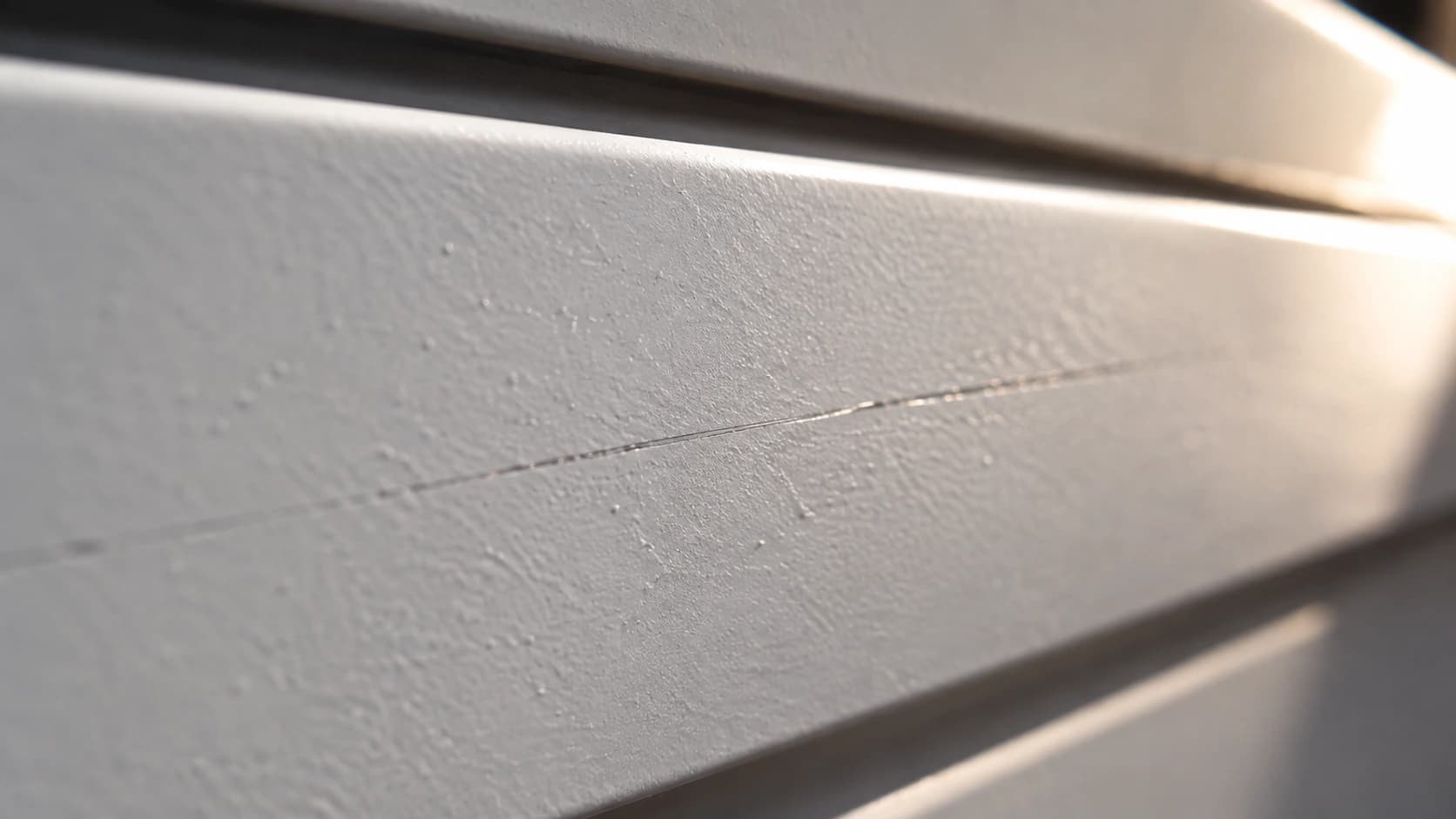 Close macro da chapa branca de um portão de alumínio pintado, com um risco fino aparecendo sob luz rasante