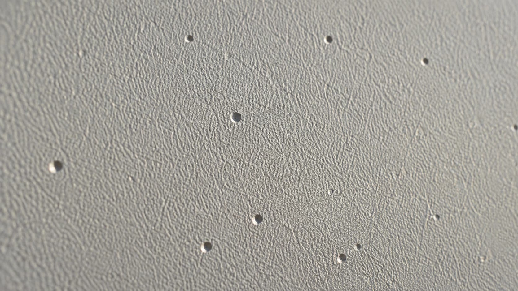 Detalhe aproximado de pequenas cavidades na chapa pintada, típicas de corrosão por pite