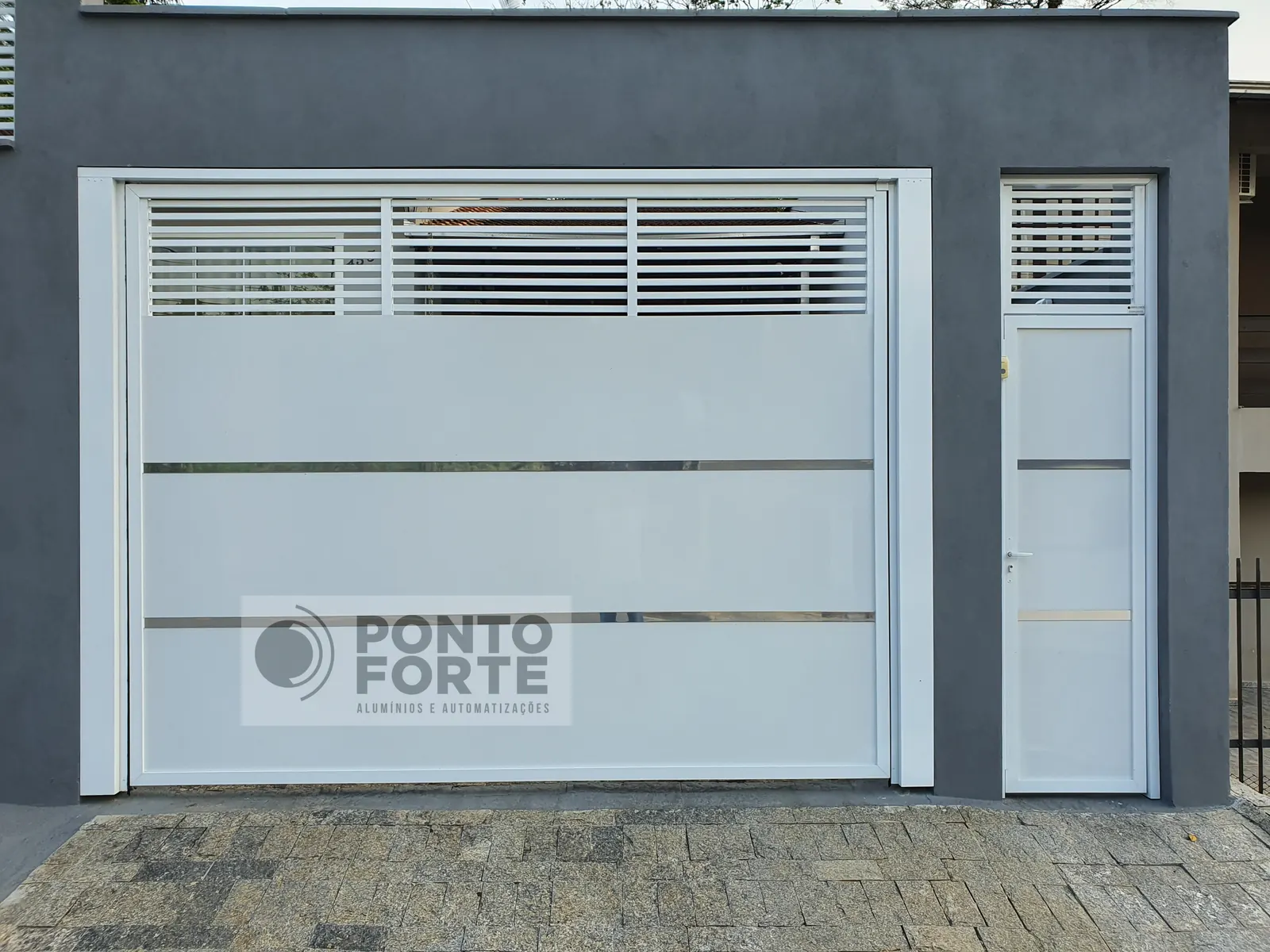 Projeto entregue pela Ponto Forte, portão basculante de alumínio branco fechado no centro e vazado em cima e embaixo, com portão social em vão próprio ao lado