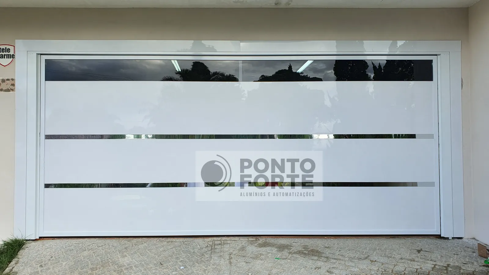 Portão basculante de alumínio branco liso com faixas cromadas, fabricado e instalado pela Ponto Forte, em Joinville