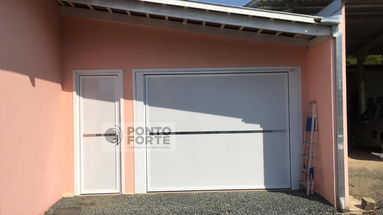 Projeto entregue pela Ponto Forte, portão basculante de alumínio branco liso, com portão social em vão próprio ao lado