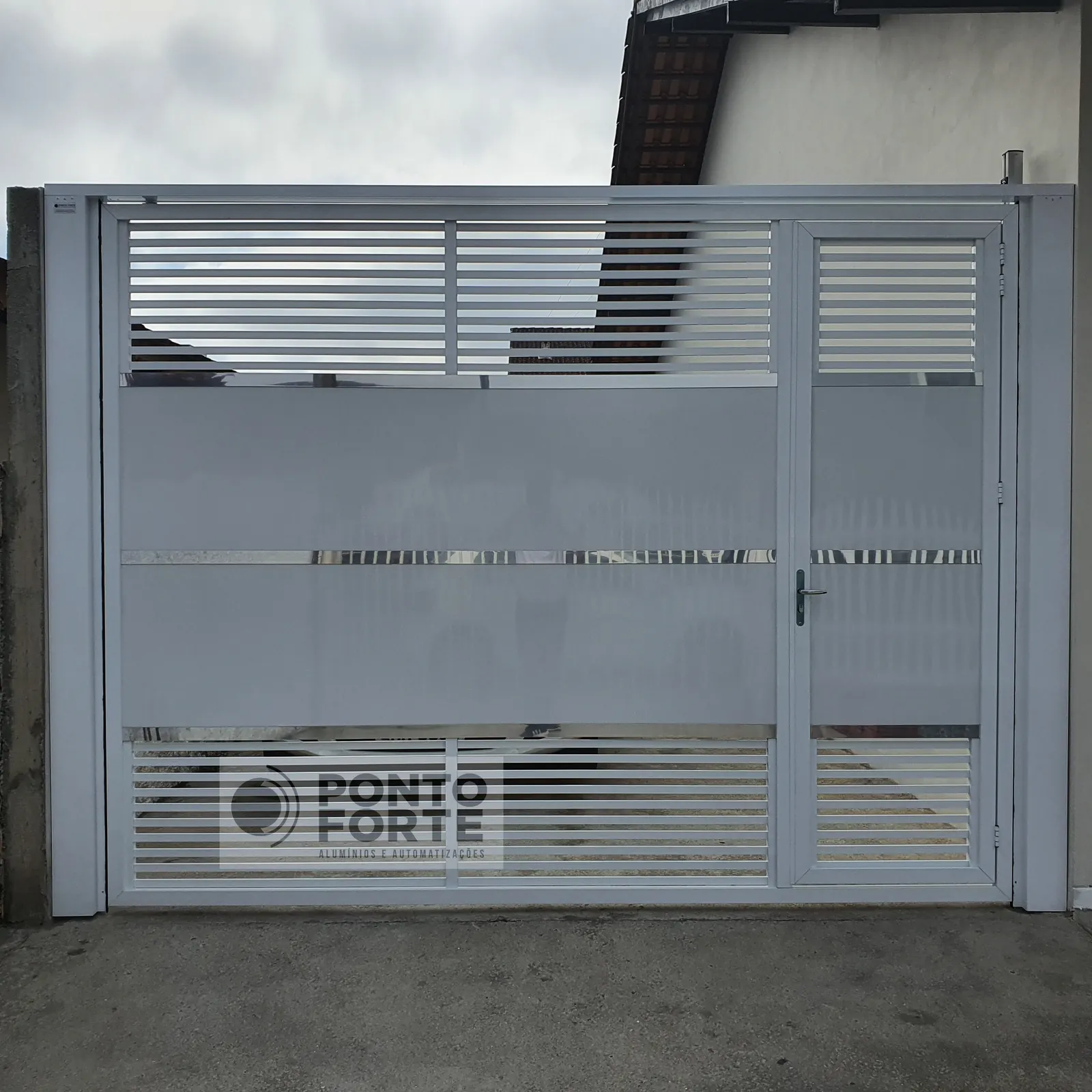 Projeto entregue pela Ponto Forte, portão basculante de alumínio branco vazado com barras horizontais, com portão social no mesmo quadro, em Joinville