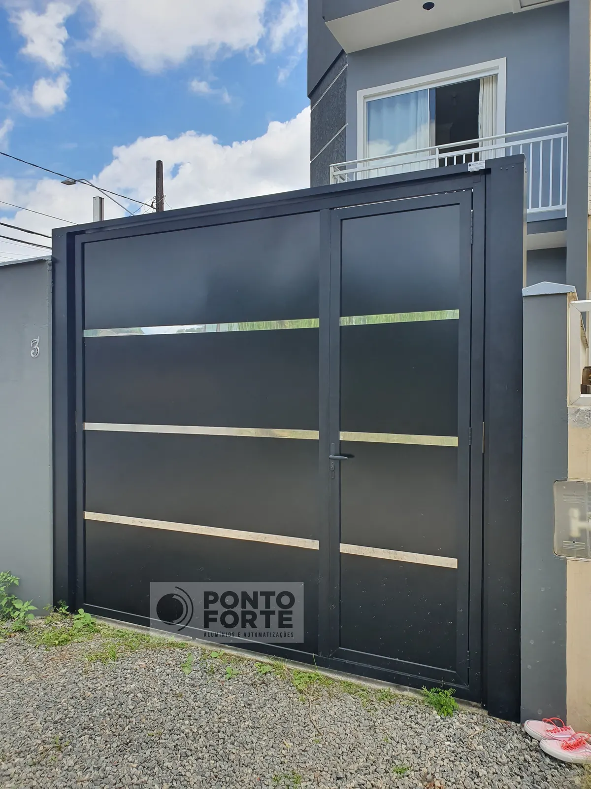 Portão basculante de alumínio preto liso com faixas cromadas, com portão social no mesmo quadro, fabricado e instalado pela Ponto Forte, em Joinville