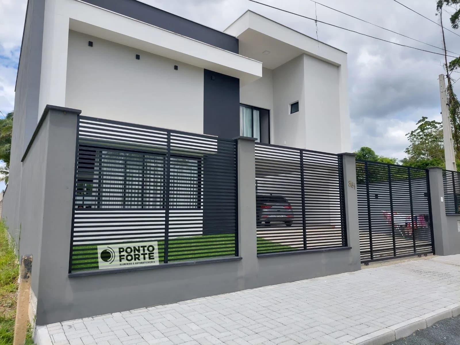 Cerca de alumínio preta vazada com barras sobre muro cinza, fechando a frente de residência moderna em Joinville