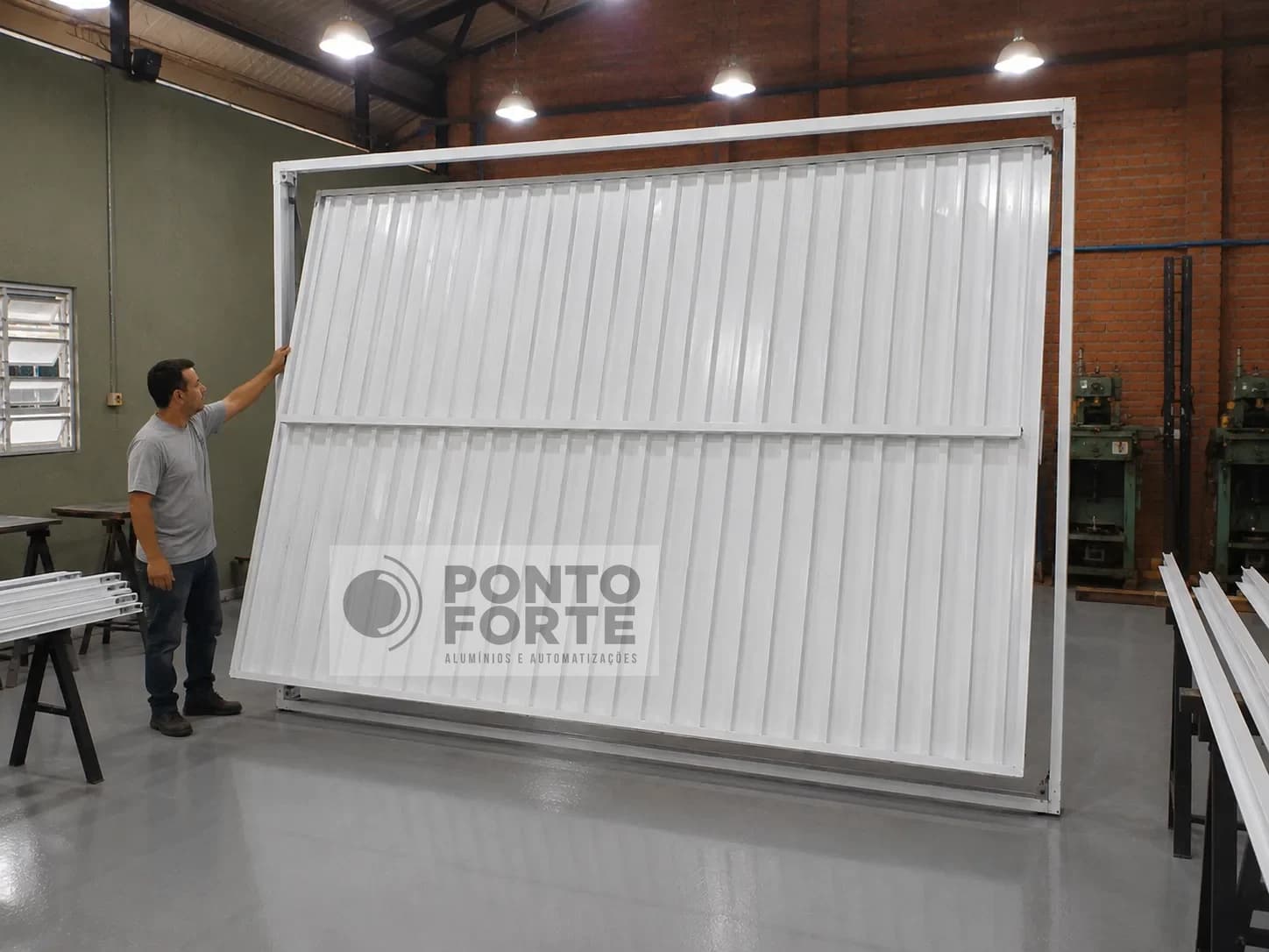 Técnico conferindo o movimento da folha de um portão basculante de alumínio branco já montado no quadro, na fábrica