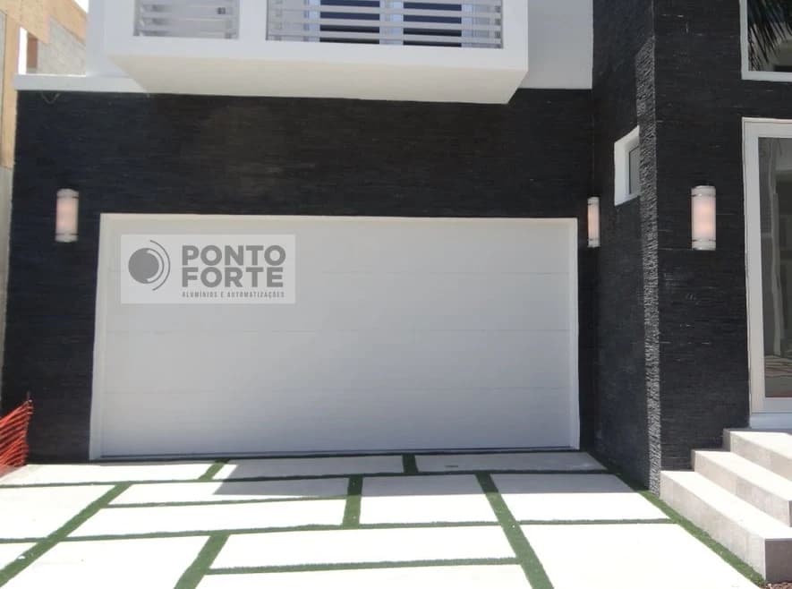 Portão basculante de alumínio branco de chapa lisa em fachada com parede de pedra