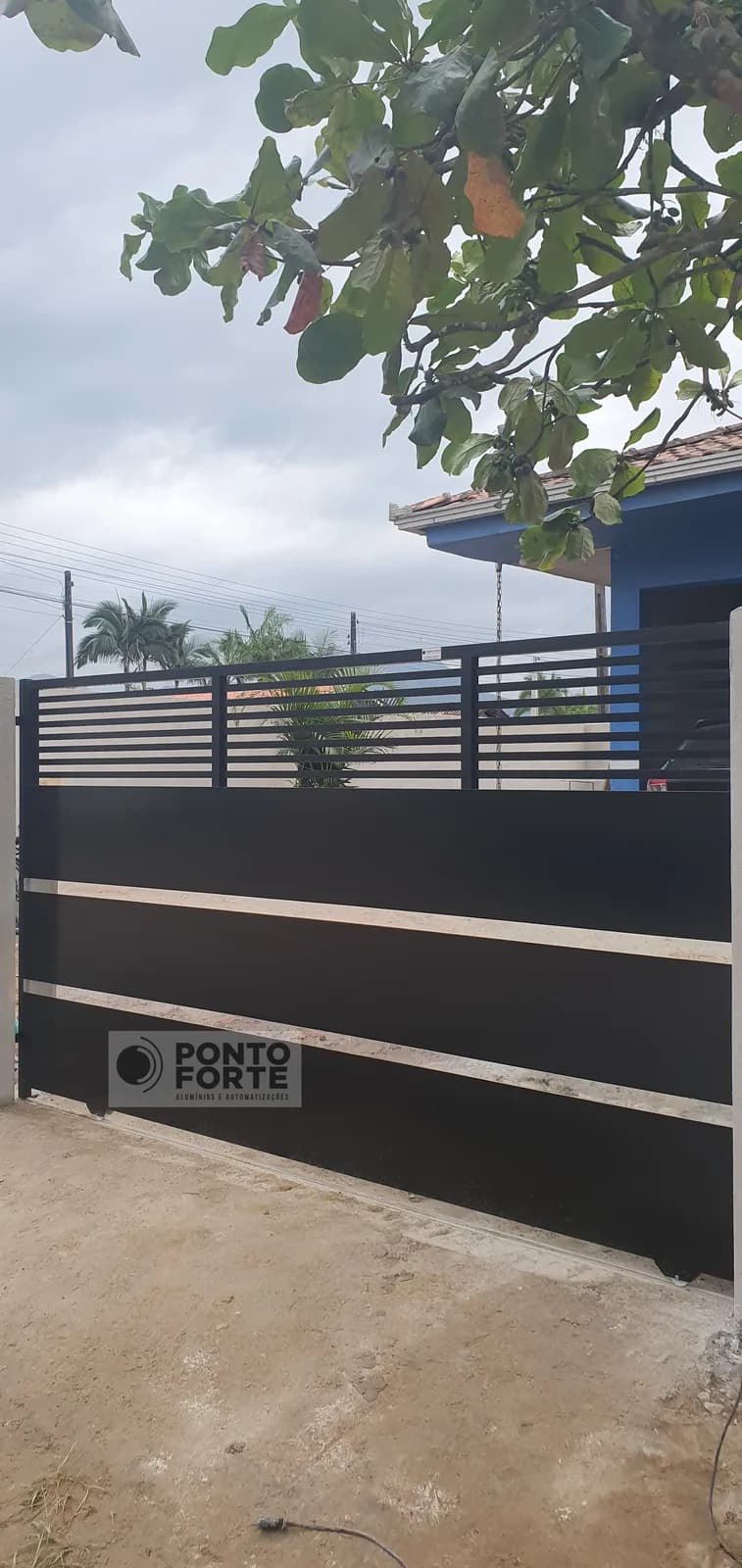 Portão de correr de alumínio preto fechado no centro, com barras vazadas na parte superior e faixas cromadas