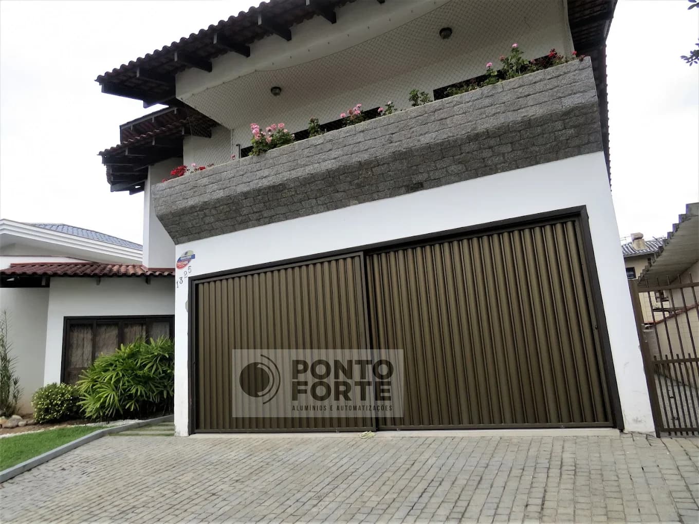 Portão de correr de alumínio bronze em lambril ripado vertical, na garagem de uma residência de dois andares em Joinville