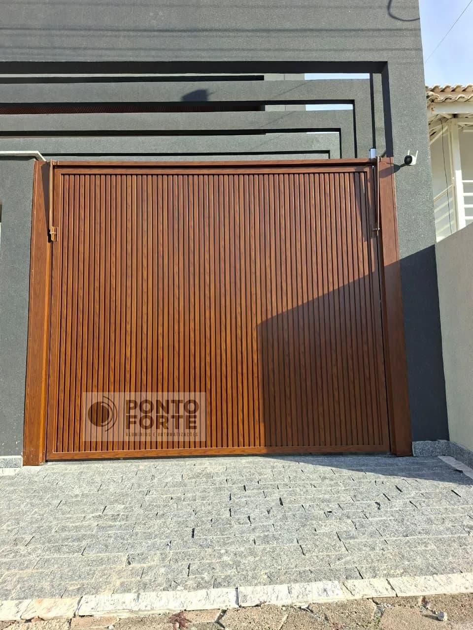 Portão basculante de alumínio amadeirado em lambril ripado vertical, com folha fechada, em residência de fachada cinza