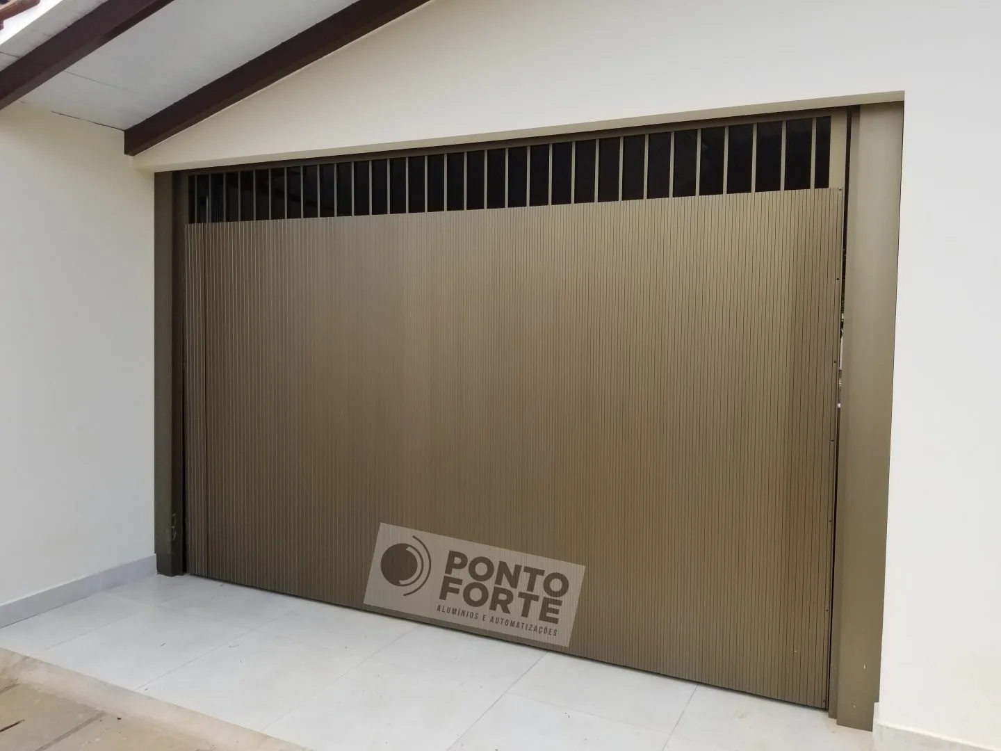 Portão basculante de alumínio amadeirado em lambril frisado vertical, visto de dentro da garagem, com faixa vazada no topo