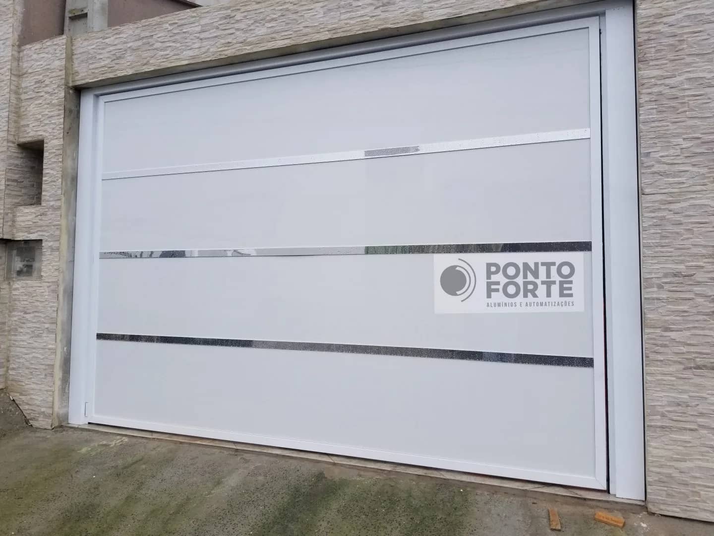 Portão basculante de alumínio branco de chapa lisa com faixas cromadas horizontais, em garagem com fachada de pedra