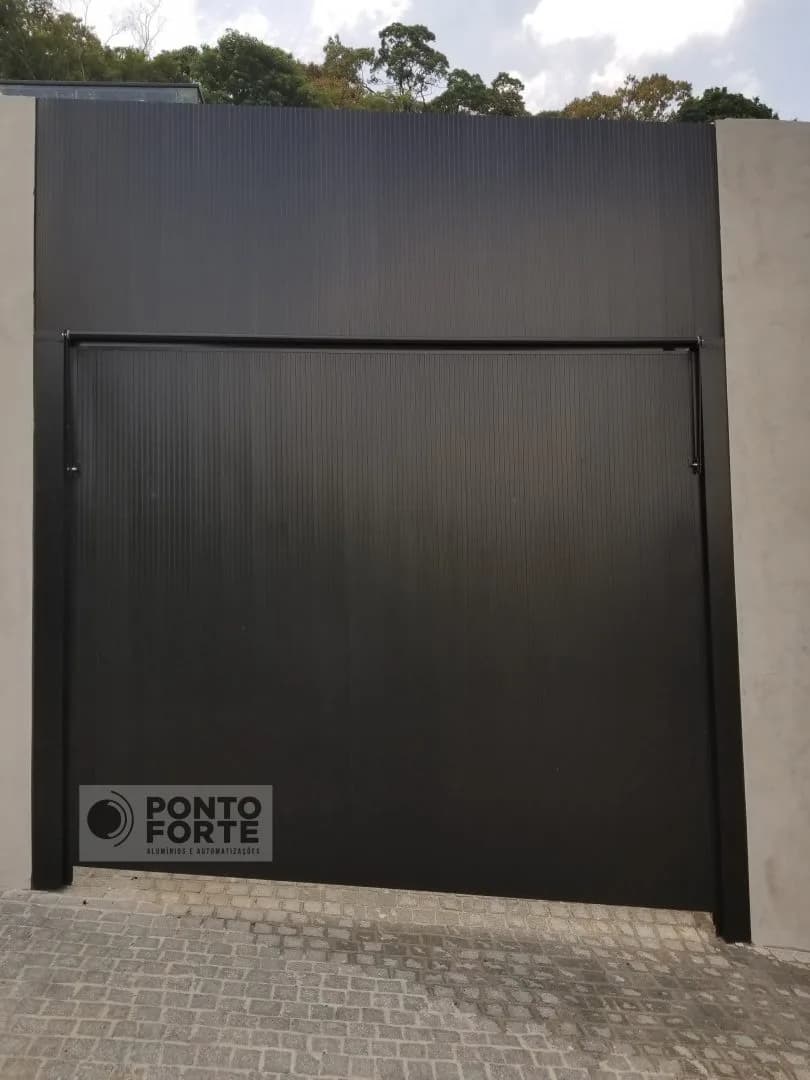 Portão basculante de alumínio preto em lambril frisado instalado em muro alto, com calçada de pedra