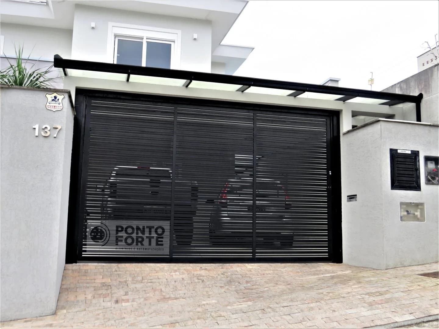 Portão basculante de alumínio preto vazado com barras finas cobrindo garagem para dois carros