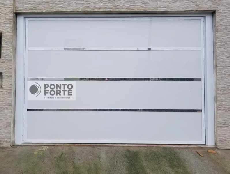 Portão de garagem de alumínio branco liso com três faixas cromadas, fechado, em fachada de pedra